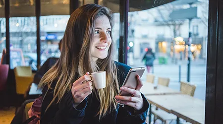 Paris, France, portrait of smiling young woman with smartphone drinking espresso in a coffee shop