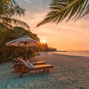 Paysage tropical de coucher de soleil, deux chaises longues, chaises longues, parasol sous palmier.  Sable blanc, vue mer avec horizon, ciel crépusculaire coloré.