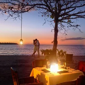 Réglage de la table romantique au premier plan avec des bougies.  Homme et femme de fond s'embrassant sous un arbre au coucher du soleil.