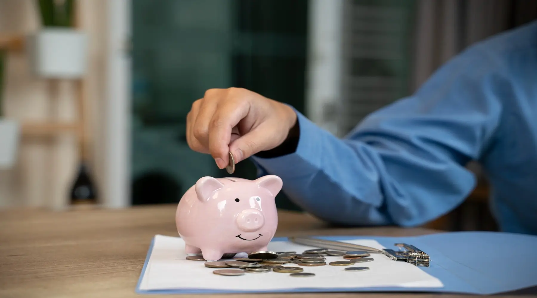 Man putting a coin into a pink piggy bank_GettyImages_1800x1000