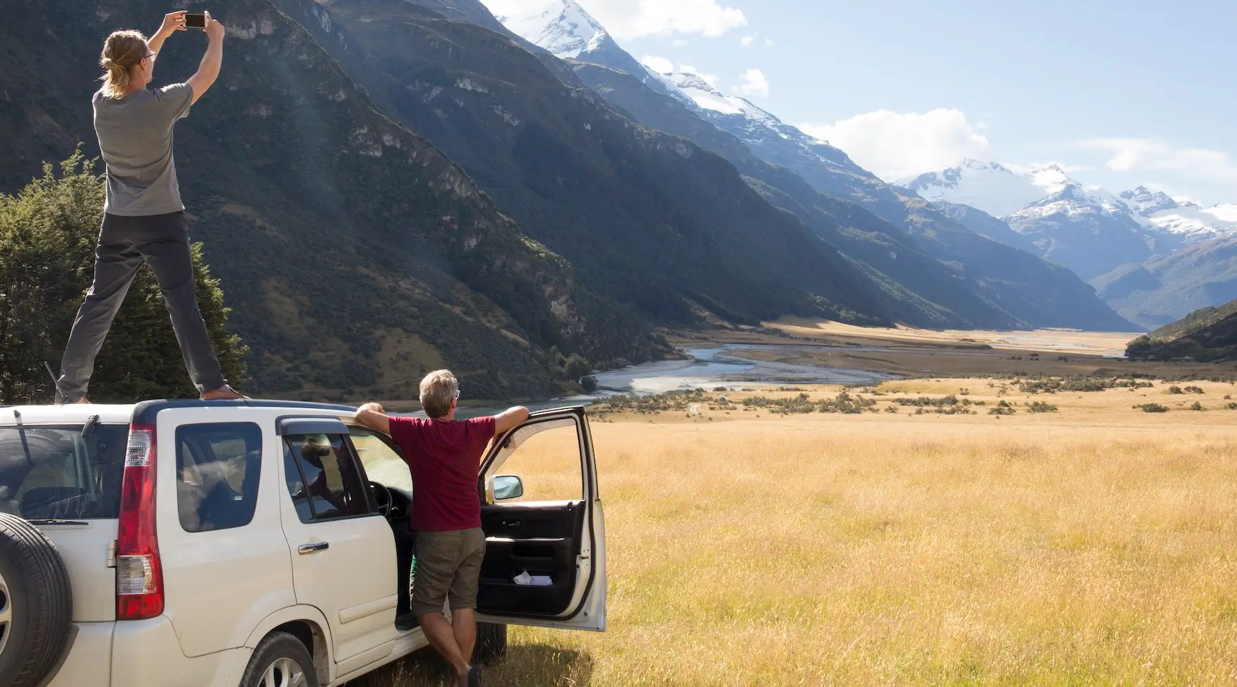 Duas pessoas ao lado de seu carro para tirar uma foto panorâmica das montanhas perto de Queenstown, Nova Zelândia.