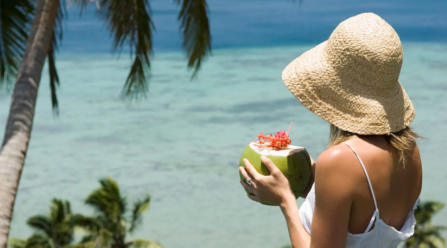 Uma mulher em Fiji olhando para o oceano e segurando uma bebida em uma casca de coco.