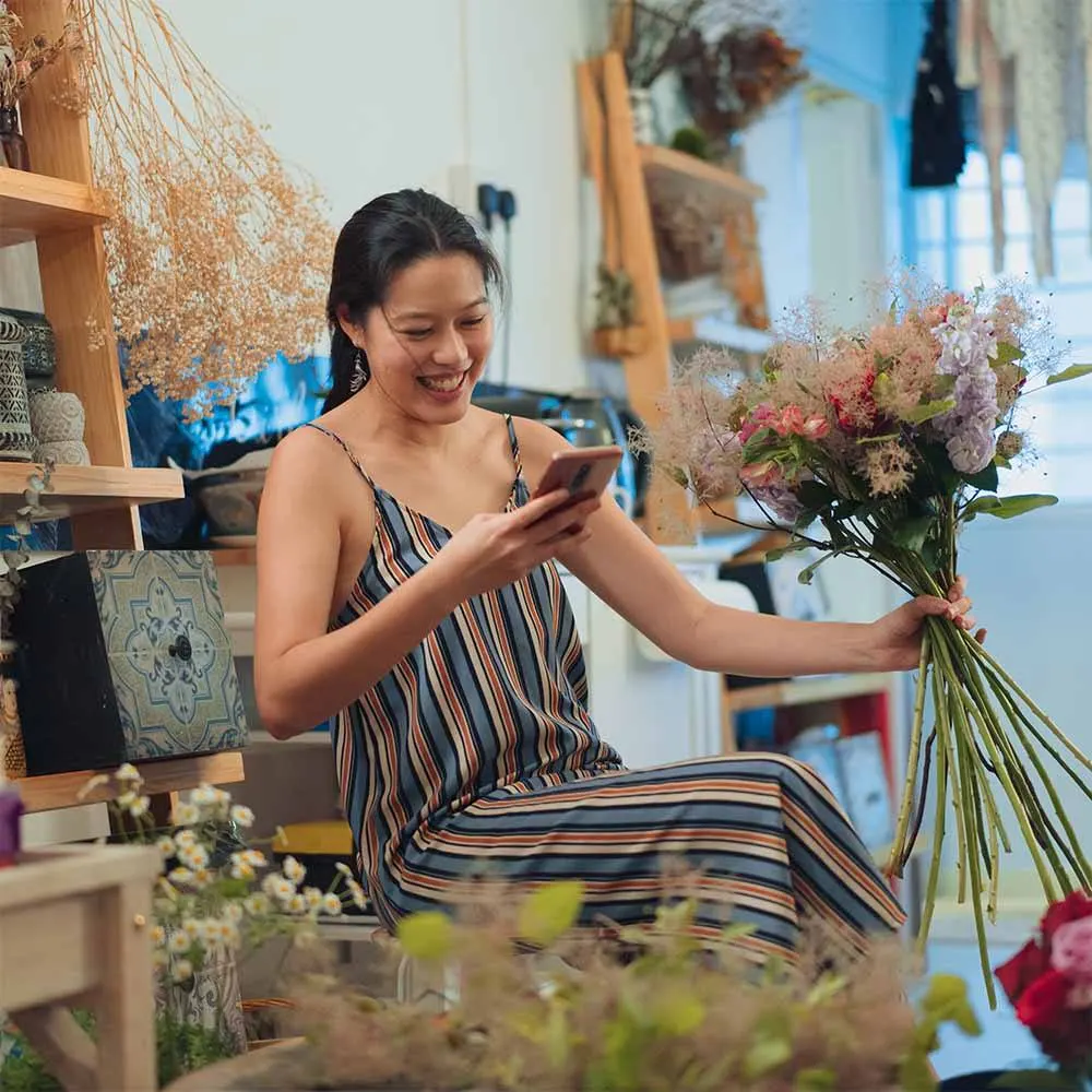 Young female florist smiling while holding flowers and phone in her hands