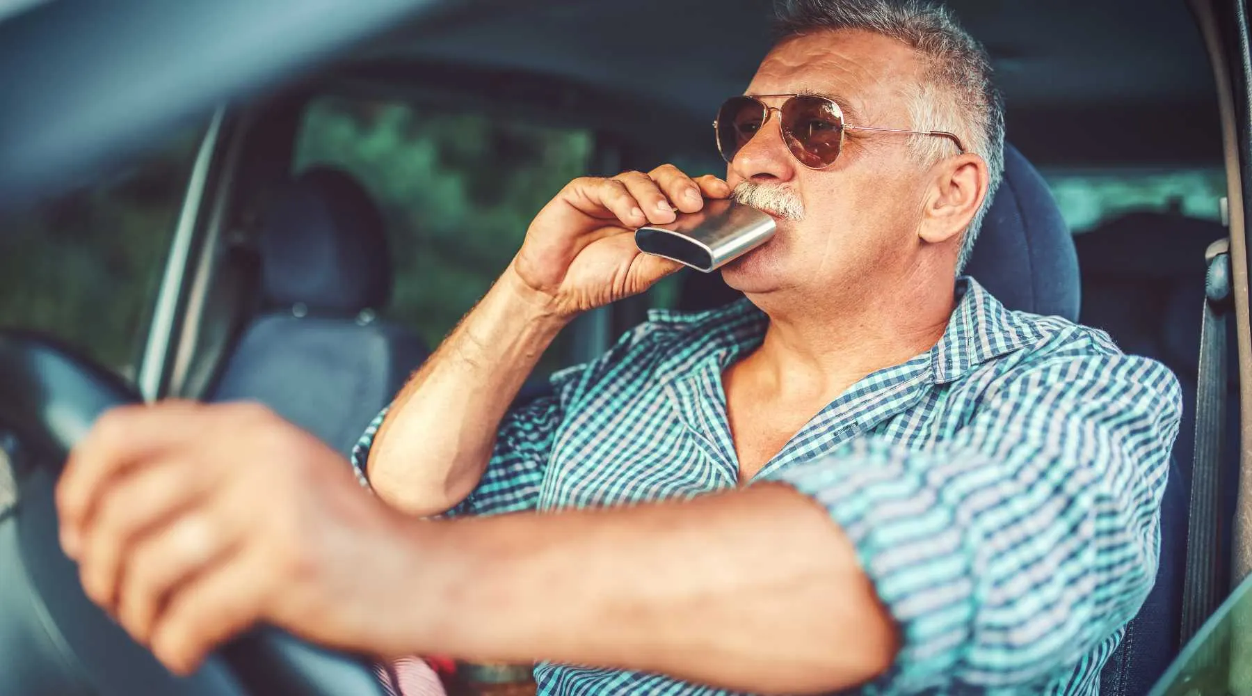 A man drinks alcohol while driving a car_Canva_1800x1000