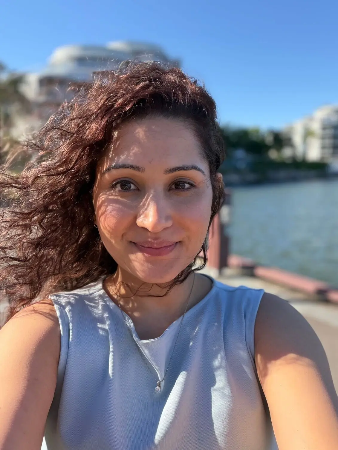 Photo using iPhone 17 close-up selfie of a woman smiling brightly in direct sunlight outdoors.