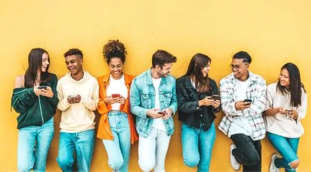 A group of friends on their phones together in front of a wall. 