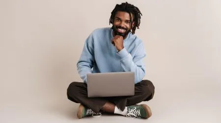A man sitting cross-legged and investing via his laptop. 