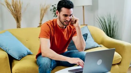 A man trading on his laptop while also using his phone. 