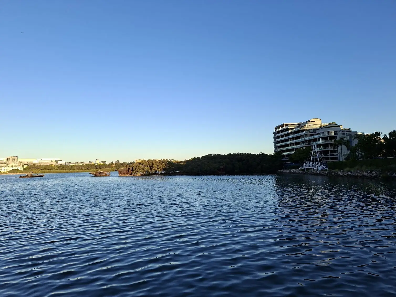 A peaceful waterfront view featuring modern apartment buildings overlooking a calm river at dusk image taken using the Samsung Galaxy A57.
