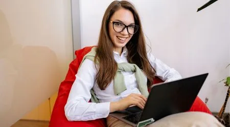 A woman investing on her laptop while she sits on a red beanbag