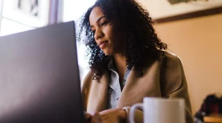A woman investing on her laptop with a cup of coffee sitting next to her