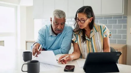 A retired couple reviewing financial documents, alongside their laptop. 