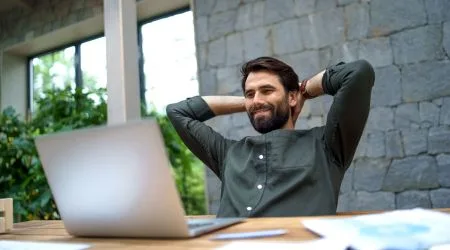 A man looking pleased as he looks at his laptop screen. 