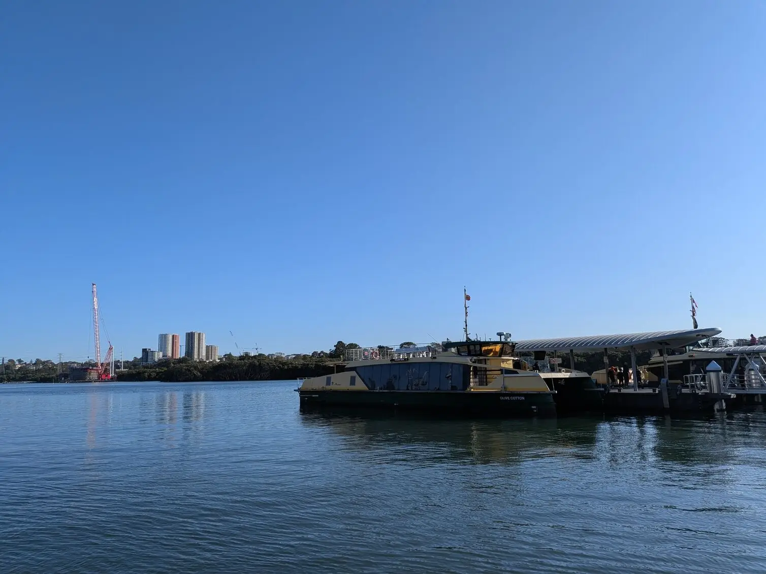 A wide daytime shot on the Google Pixel 10a of a docked ferry against a clear blue sky and distant city skyline.