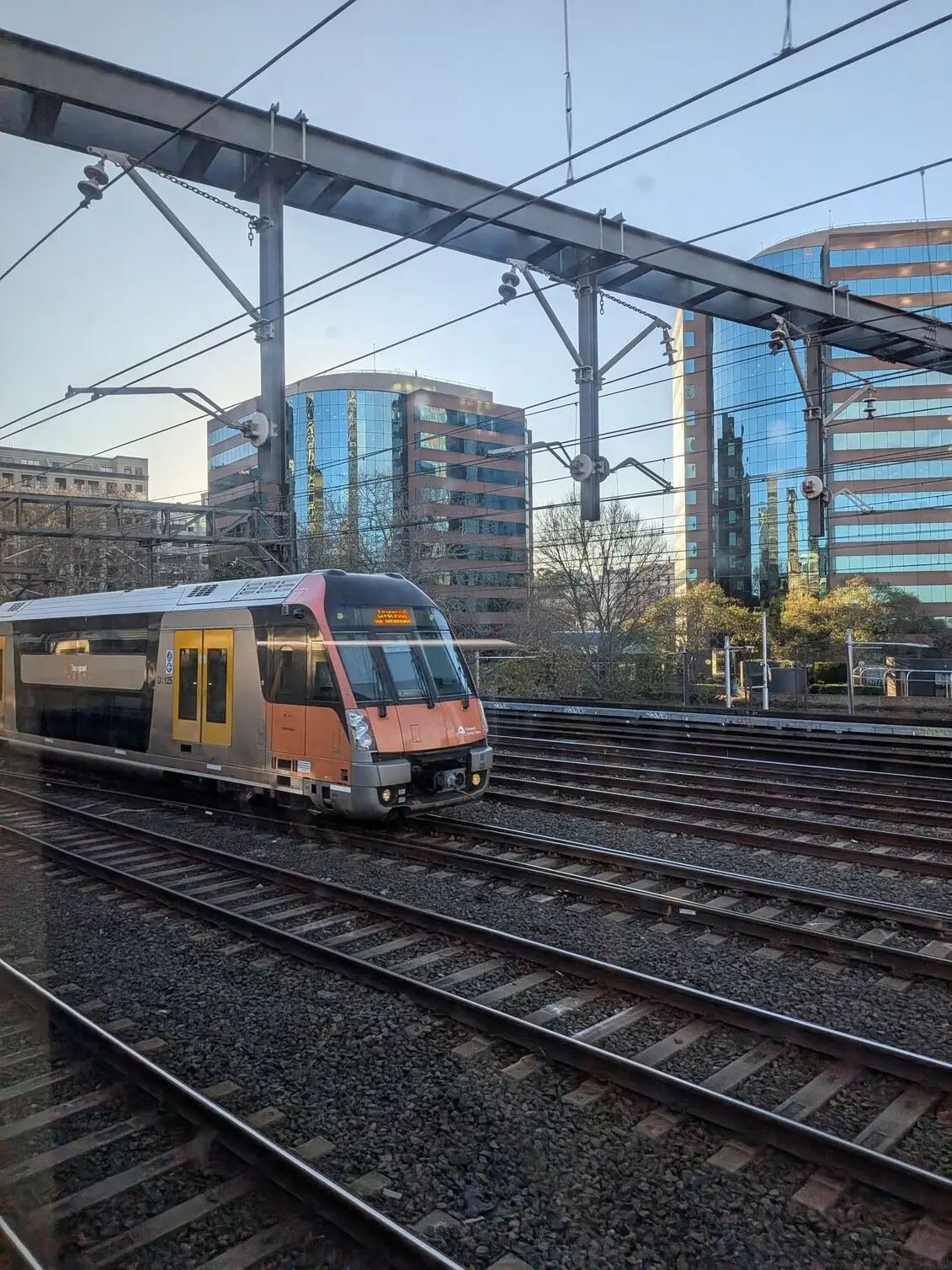 Google Pixel 10a captures a Trains service in motion, framed by overhead wires and glass office towers.