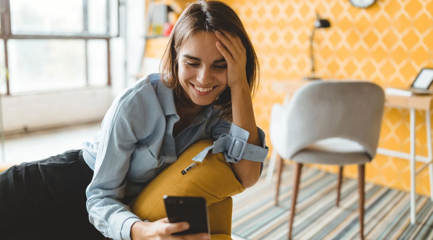 Happy_Woman_Looking_Smartphone_Orange_Room_Canva_1800x1000
